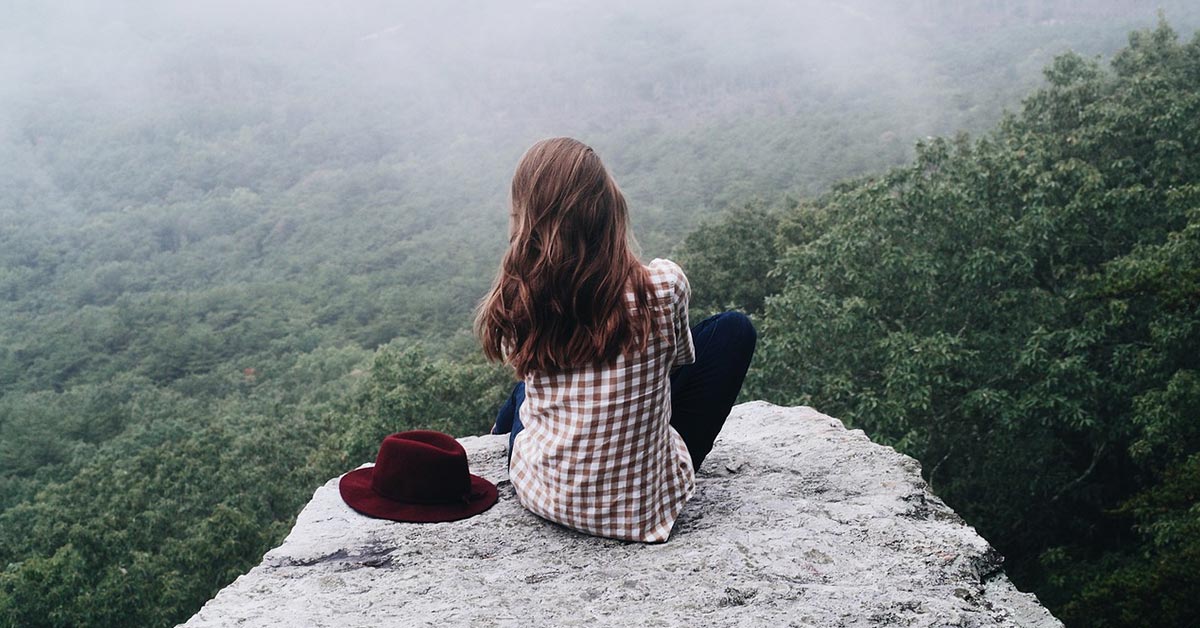 Tiefe Heilung und Neubeginn, Bindungscoaching KlarRaum Junge Frau sitzt auf einem Felsen und blickt über die Landschaft