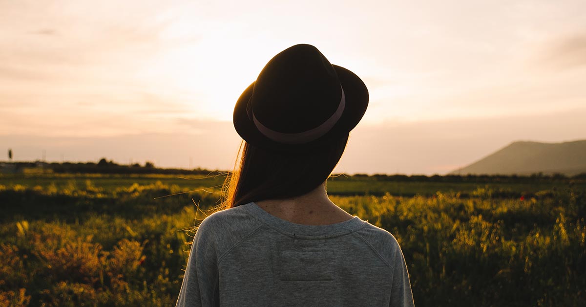 Zurück in Verbindung, KlarRaum Coaching Junge Frau blickt auf eine Wiese bei Sonnenaufgang