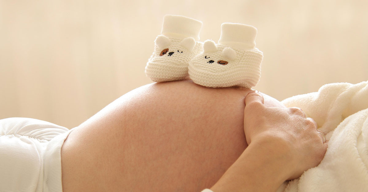Vortrag: Gemeinsam wachsen, von Anfang an Der Bauch einer Schwangeren mit kleinen Babyschühchen